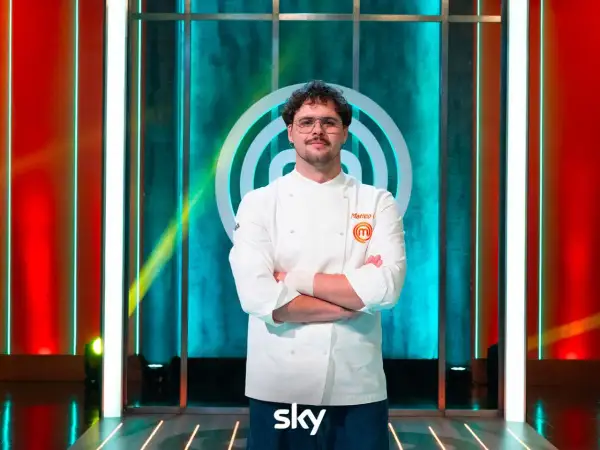 Matteo, vincitore MasterChef 15, posa con la sua divisa da chef, braccia conserte, sullo sfondo del logo del programma.