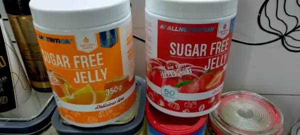Dwie puszki galaretki bez cukru: pomarańczowa i truskawkowa. Zastanawiasz się, ile kalorii ma galaretka truskawkowa? Te produkty są niskokaloryczne.