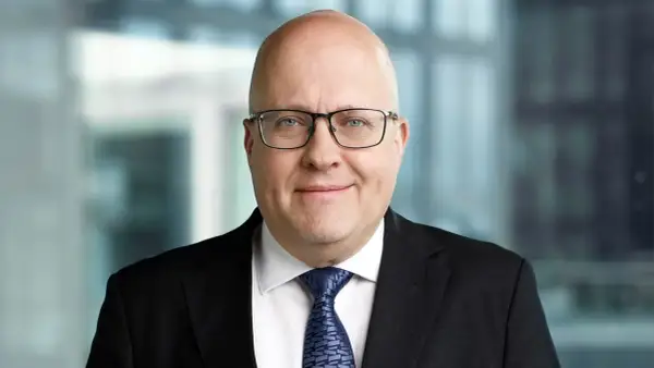 Mikael Staffas, en man med glasögon och kostym, ler mot kameran.
