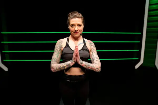 A tattooed woman in athletic wear holds her hands in prayer pose, ready for yoga for boxers.