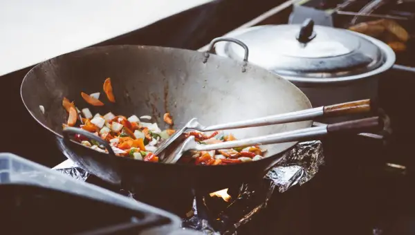 Wok med grönsaker som steks, med olika peppar sorter som ger smak. En gryta står i bakgrunden.