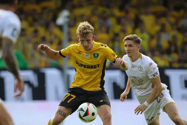 Piłkarz KS Pegaz Chwałowice w żółtej koszulce z numerem 77 drybluje, a obok niego biegnie przeciwnik w białej.
