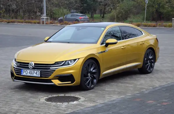 Złoty Volkswagen Arteon R z czarnym dachem i felgami, zaparkowany na bruku.