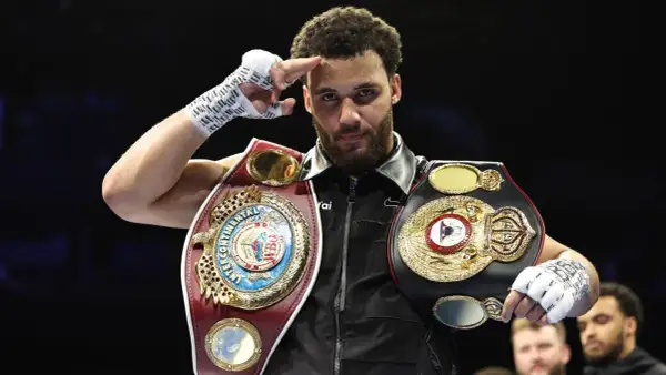 A boxer, champion of the super flyweight weight class, salutes with his championship belts.