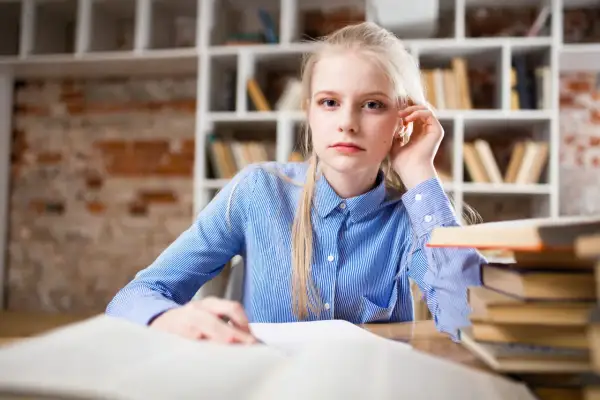 Młoda kobieta z blond włosami siedzi przy biurku, przed nią otwarte księgi. Przygotowuje wniosek o zwolnienie z kosztów sądowych.