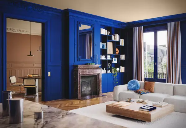 Un soggiorno elegante con pareti blu intenso, camino in marmo, libreria e divano bianco. Un'altra stanza con tavolo e sedie è visibile attraverso un'apertura.