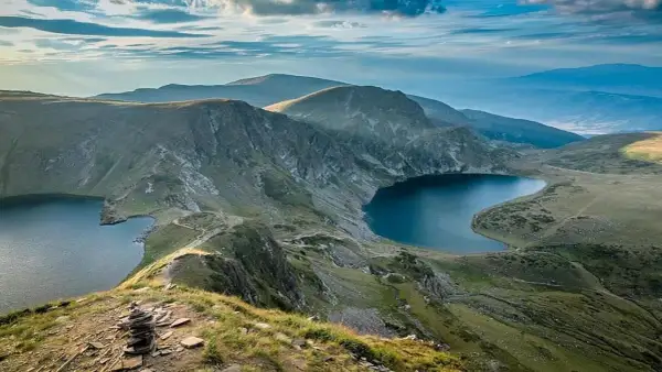 Vue panoramique d'un trek en Bulgarie. Des lacs glaciaires d'un bleu profond bordent des montagnes verdoyantes sous un ciel nuageux.