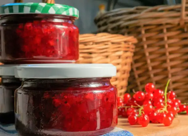 Słoiki z domowym dżemem z porzeczki czerwonej, obok świeże owoce. W tle plecione kosze.