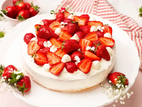 Eine köstliche Erdbeer-Sahne-Torte, üppig belegt mit frischen Erdbeerscheiben und Sahnetupfern, verziert mit kleinen weißen Blüten.
