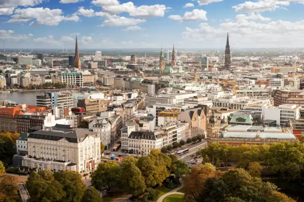 Blick von einer **Aussichtsplattform Hamburg** über die Stadt mit ihren Kirchtürmen, dem Hafen und grünen Bäumen im Vordergrund.