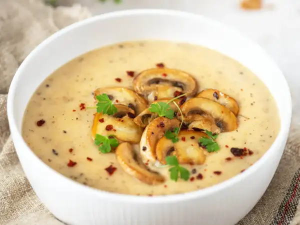 Aksamitny zupa krem z pieczarek, udekorowana plasterkami pieczarek, natką pietruszki i płatkami chili.