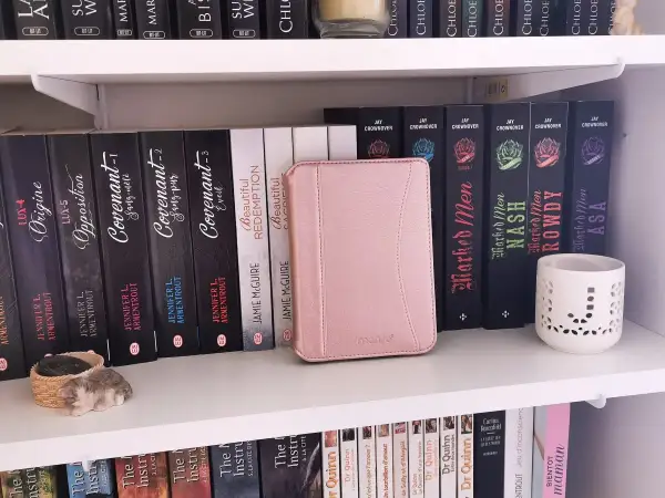 Une liseuse Kobo rose est bloquée en veille, posée sur une étagère remplie de livres.