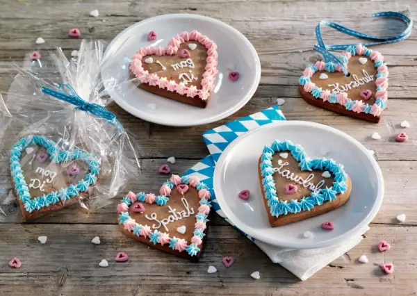 Bunte Lebkuchenherzen selber machen: mit Zuckerguss und Sprüchen verziert, liegen sie auf Holztisch.