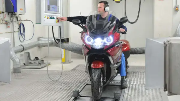 Mężczyzna w słuchawkach obsługuje motocykl na hamowni.