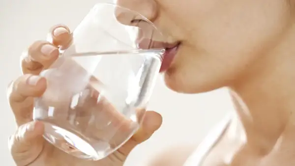Une femme boit un verre d'eau. Une question importante pour les jeunes mamans : quelle eau boire allaitement ?