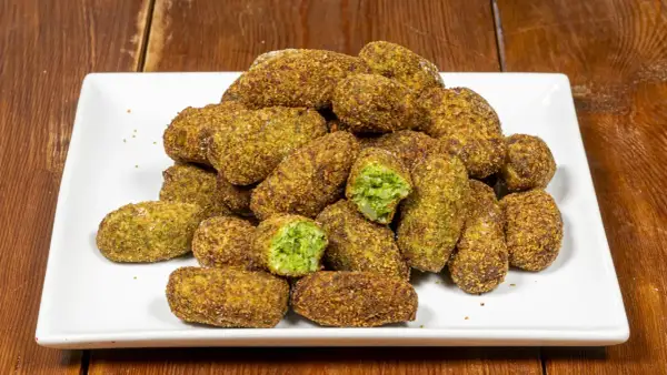 Un mucchio di polpette di broccoli dorate e croccanti su un piatto bianco. Alcune sono tagliate a metà, rivelando il ripieno verde brillante.