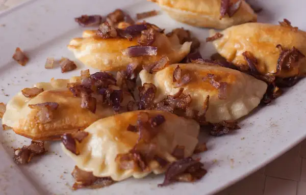 Pyszne pierogi z mięsem, posypane chrupiącą cebulką, kuszą swoim wyglądem.