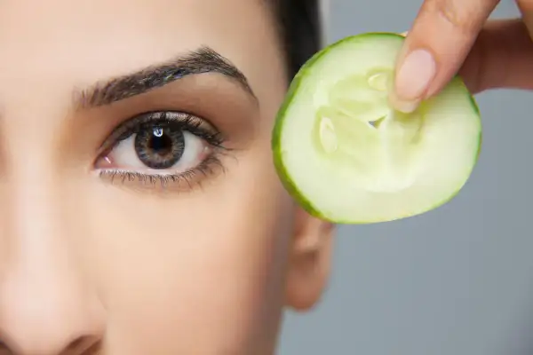 Une tranche de concombre est tenue près de l'œil, une méthode naturelle pour enlever les poches sous les yeux.