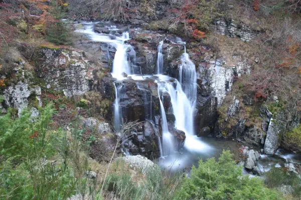 Il sentiero delle cascate serpeggia tra rocce e foliage autunnale, con l'acqua che scende impetuosa.