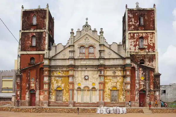 Façade d'une église à Porto-Novo, aux tours jumelles imposantes et à la peinture écaillée, avec des enfants jouant devant.