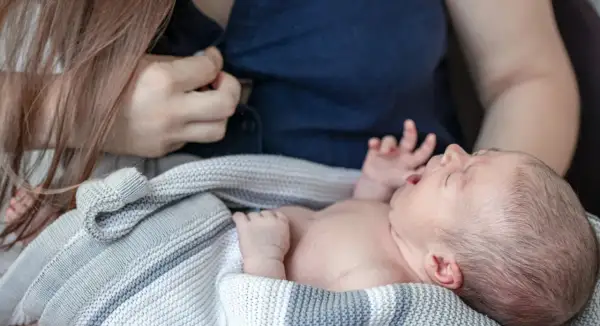 En bebis frustrerad vid amning, med öppen mun och knutna händer, insvept i en stickad filt.