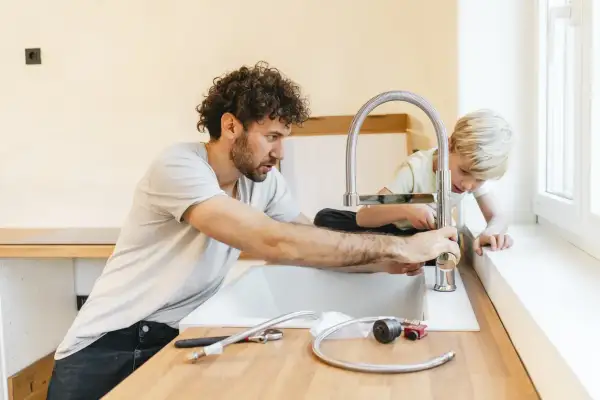 Padre e figlio installano un nuovo rubinetto in cucina, un'operazione che richiede attenzione per spostare attacchi cucina senza rompere pavimento.