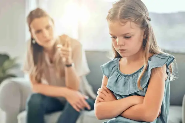 Een meisje met gekruiste armen toont duidelijk oppositioneel gedrag, terwijl haar moeder op de achtergrond met haar vinger waarschuwt.