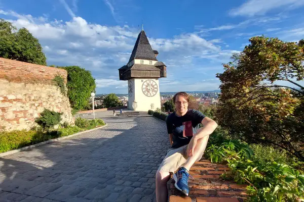 Mann sitzt vor dem Uhrturm in Graz. Ein toller Ort für graz geheimtipps mit Blick über die Stadt.