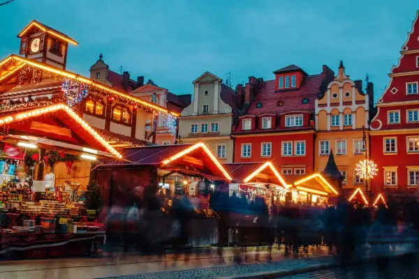 Bunte Häuser und beleuchtete Stände auf dem Wroclaw Weihnachtsmarkt. Menschen schlendern durch die festliche Atmosphäre.