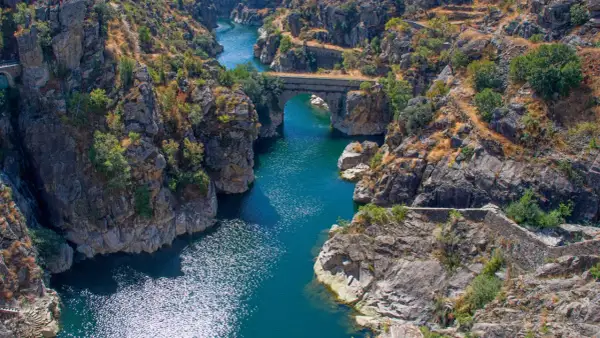Cañón con río azul y puente de piedra, evocando la belleza natural de los pueblos de Madrid.