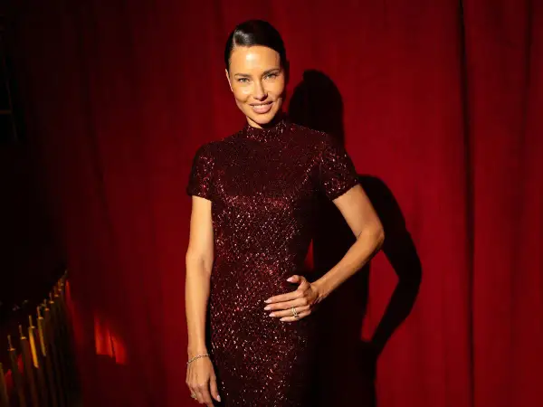 Adriana Lima actual, deslumbrante con un vestido de lentejuelas borgoña, posa con confianza ante un telón de terciopelo rojo.