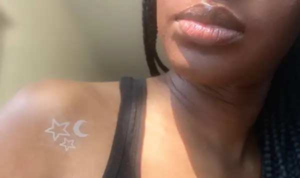 Un delicado tatuaje de tinta blanca con estrellas y luna sobre piel negra, un toque celestial sutil.