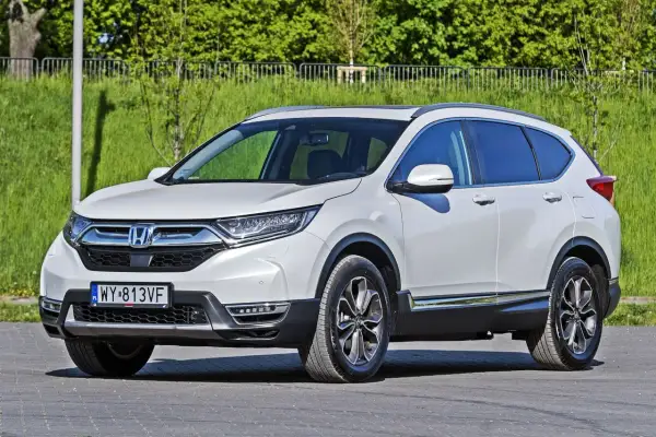 Biała Honda CR-V zaparkowana na zewnątrz, z zielenią w tle.