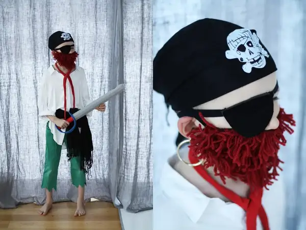 Dziecko w stroju pirata 122: czarna bandama z czaszką, opaska na oko, czerwona broda z włóczki, biała koszula, zielone spodnie i miecz.