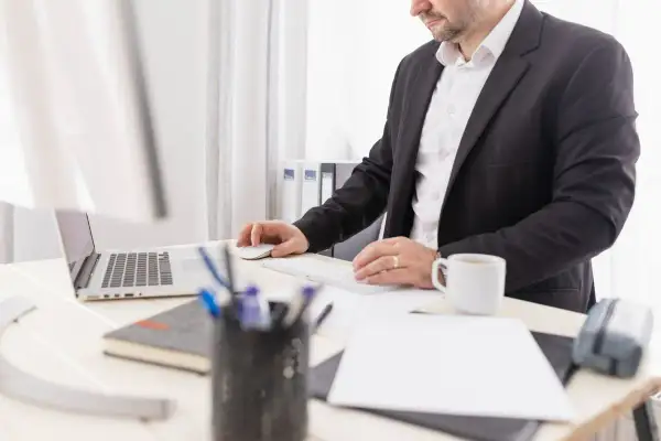 Biznesmen przy biurku, pracujący przy laptopie i klawiaturze. Może to być związane z wpłatą gotówki na konto firmowe.