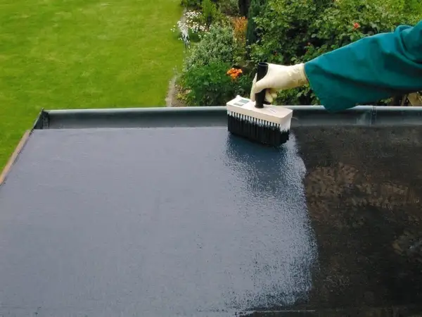 Mit einem Pinsel wird ein Bitumen-Voranstrich auf eine flache Dachfläche aufgetragen.