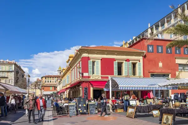 En livlig marknad i en nice gamla stan med färgglada byggnader, uteserveringar och folk som strosar.