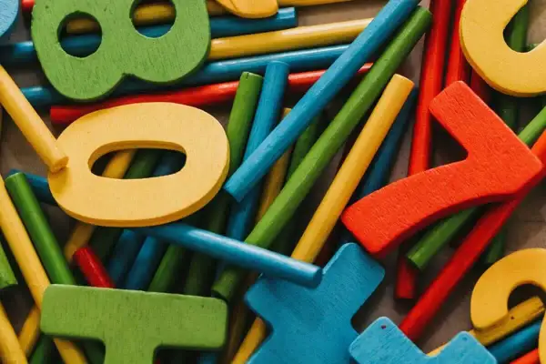 Bunte Holzfiguren und Stäbchen, die ein Helfersystem Grundschule bilden. Zahlen wie 0, 7 und 8 sind erkennbar.