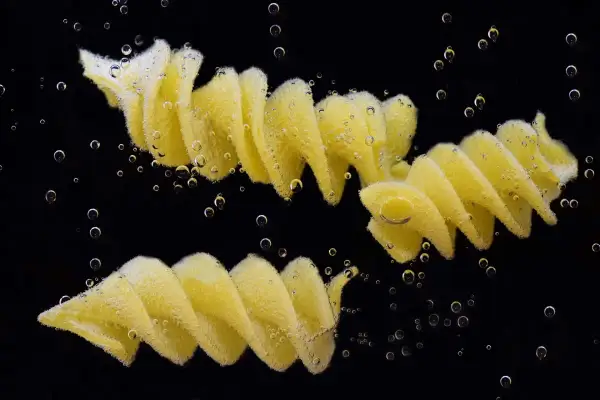 Dwa makarony fusilli gotujące się w wodzie, otoczone bąbelkami. Idealny przykład, jak ugotować makaron.
