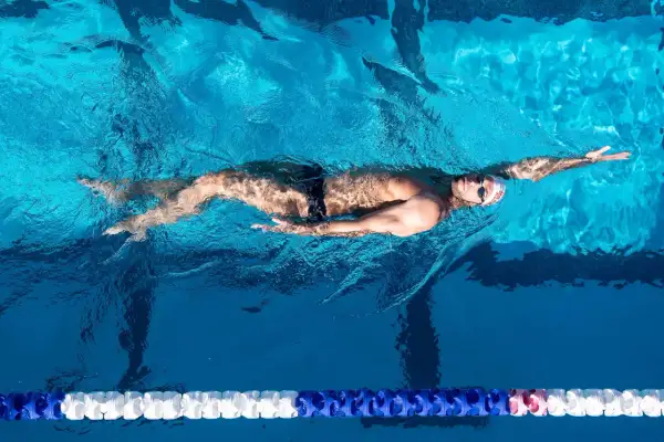 A male backstroke swimmer glides through the bright blue water of a pool, his body streamlined and arms extended.