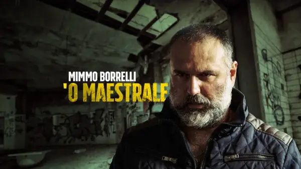 Mimmo Borrelli, 'O Maestrale, in un'ambientazione che ricorda Gomorra, con graffiti e un'atmosfera cupa.