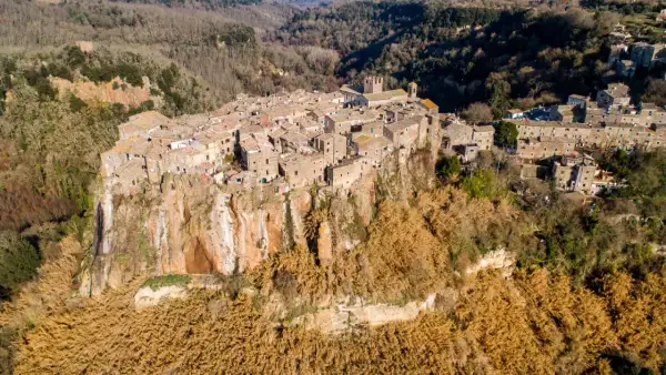 Antico borgo di Calcata Viterbo arroccato su una rupe tufacea, circondato da vegetazione secca e boschi.