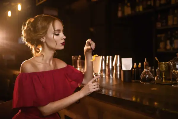 Elegancka kobieta w bordowej sukience z koktajlem w dłoni, idealne paznokcie do bordowej sukienki.