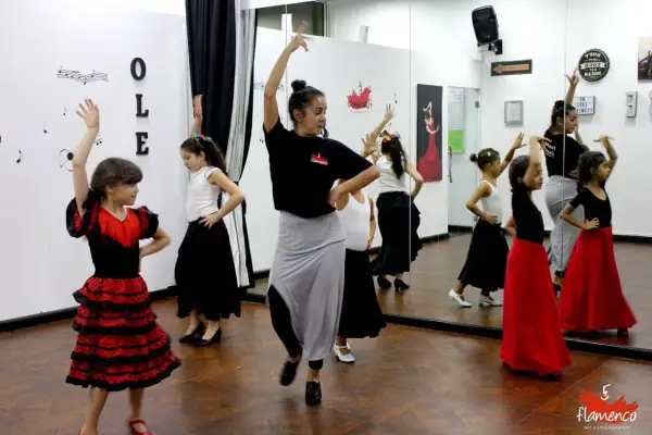 Niñas aprenden baile flamenco en una clase. La maestra las guía con movimientos elegantes.