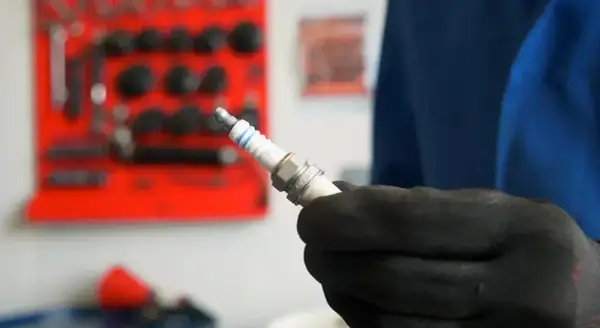Main tenue une bougie d'allumage neuve, prête à être installée. Savoir quand changer les bougies d'allumage est essentiel pour le bon fonctionnement de votre moteur.