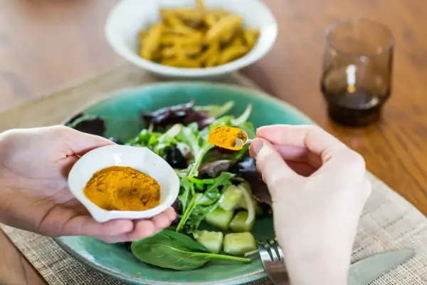 Mani aggiungono curcuma a un'insalata, sfruttando i curcuma e pepe nero benefici per un pasto sano.