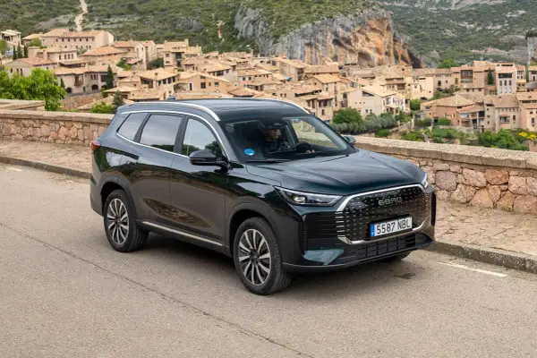 Ebro S800 PHEV, un SUV moderno, aparcado en una carretera con un pueblo pintoresco de fondo.