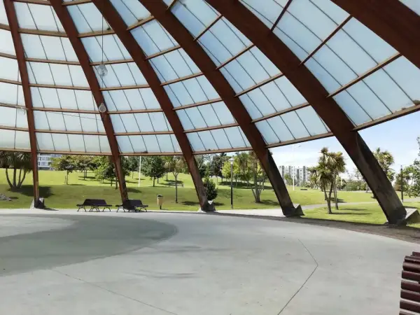 Estructura de madera y cristal en el parque de Eiris, con vistas a césped, árboles y edificios.