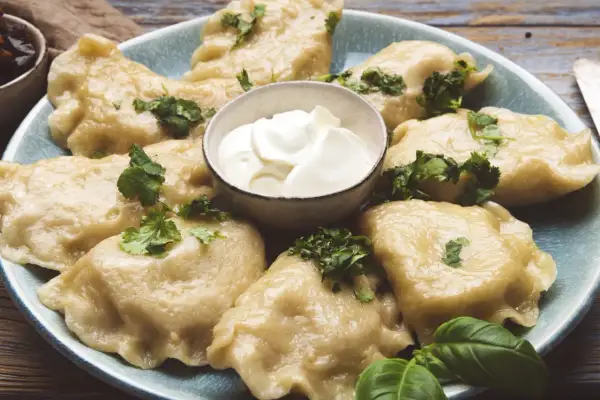 Pyszne pierogi ze szpinakiem i serem feta, udekorowane natką pietruszki, podane z kleksem śmietany.