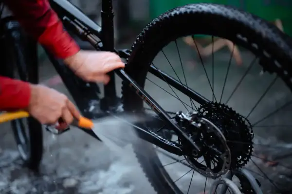 Iemand maakt de fietsketting schoon met Dasty, terwijl de rest van de fiets nat wordt gespoten.